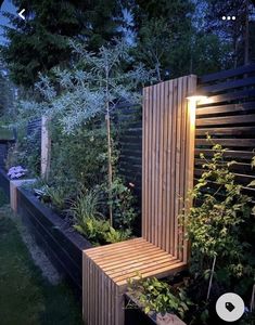 a wooden bench sitting in the middle of a lush green garden at night with lights on