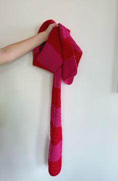 a person is holding a pink and red knitted scarf on the wall with their hand