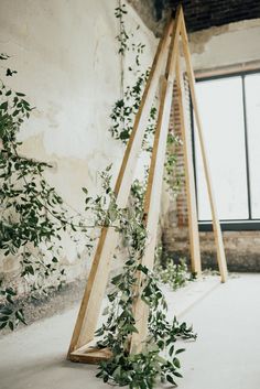 an art installation made out of wood and greenery in front of a large window