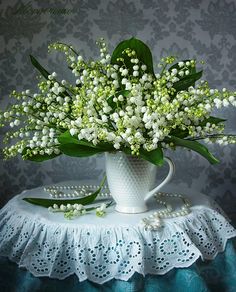 a white vase filled with flowers sitting on top of a lace covered table cloth next to a wall