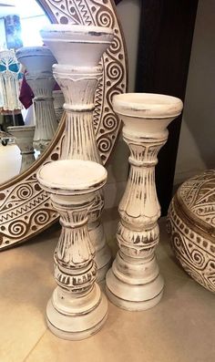 three white candlesticks sitting on top of a counter next to a round mirror