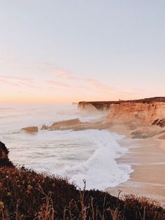 the beach is next to some cliffs and waves crashing on it's shore as the sun sets