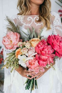 a woman holding a bouquet of pink and white flowers in her hands with greenery