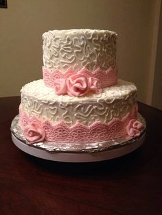 a three tiered cake with pink flowers on the top and white frosting, sitting on a table