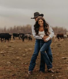 a man and woman hugging in the middle of a field with cows behind them on a cloudy day