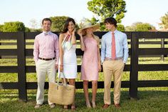 four people standing next to each other in front of a wooden fence with grass and trees