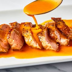 a spoon drizzling sauce onto some meat on a white plate with orange sauce