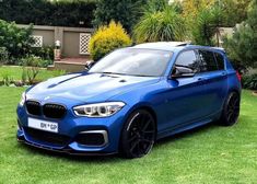 a blue bmw car parked on top of a lush green grass covered field next to trees