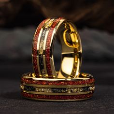 two gold rings with red and black glitters on them, sitting next to each other