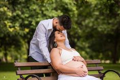 a pregnant woman sitting on top of a wooden bench next to a man in a white shirt