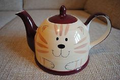 a ceramic tea pot with a cat design on the front and sides, sitting on a couch