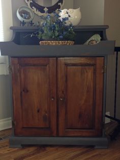 a wooden cabinet sitting on top of a hard wood floor next to a mirror and vase