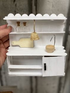 a hand holding a miniature doll house with shelves