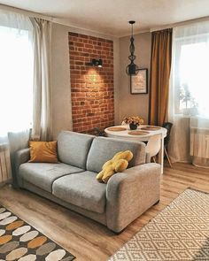 a living room filled with furniture and a brick wall behind the couch, next to a dining table