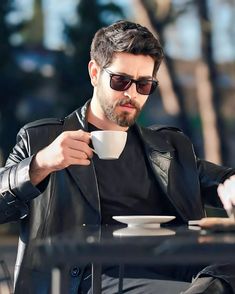 a man sitting at a table holding a cup and saucer in his hand while wearing sunglasses