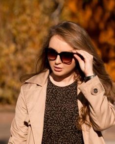 a woman walking down the street with her hand on her head while wearing sunglasses and a trench coat