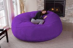 a woman sitting on a large purple bean bag chair in front of a fire place