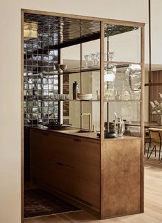 a kitchen with wooden cabinets and glass shelves on the wall, in front of a dining room table