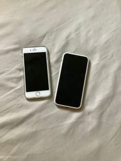 two cell phones sitting on top of a bed next to each other in front of a white sheet