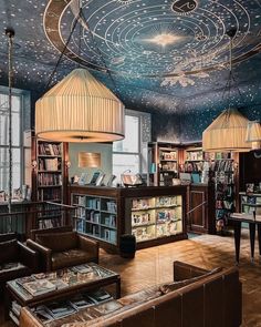 a library with many books on shelves and lamps hanging from the ceiling over it's seating area