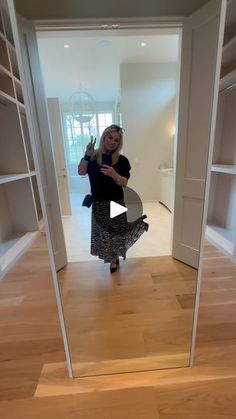 a woman taking a selfie in front of an open door with shelves behind her