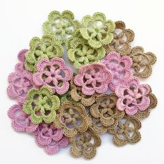 several crocheted flowers are arranged together on a white surface, one is green and the other is pink