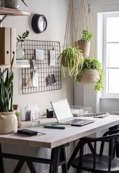 a laptop computer sitting on top of a wooden desk next to a plant hanging from the wall