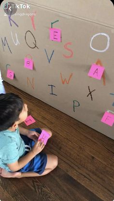 a little boy sitting on the floor playing with some pink sticky notes that spell out words