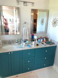 a bathroom with blue cabinets and white counter tops is seen in this image, while the woman takes a selfie in the mirror