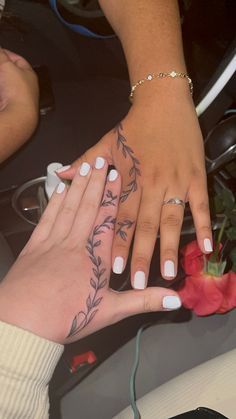 two hands with flowers on their fingers and one has a rose tattooed on the other hand