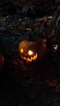 two jack o lantern pumpkins sitting on the ground with their faces glowing in the dark