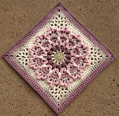 a crocheted square with pink and white flowers on it sitting on the ground