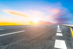 the sun is setting on an empty highway with white lines and yellow markings in the middle