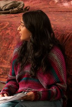 a woman sitting on a bed looking off into the distance with a book in her hand