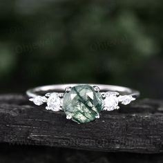 a green and white diamond ring sitting on top of a piece of wood with leaves in the background