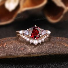 a red and white diamond ring sitting on top of a piece of wood next to flowers