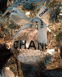 a chanel ornament hanging from a christmas tree with ornaments around it and ribbon