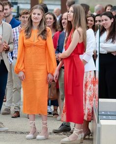 two women in orange dresses standing next to each other with people watching them from the sidelines