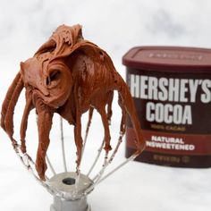 a whisk with chocolate frosting on it next to a container of hershey's cocoa