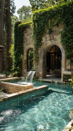 an outdoor swimming pool surrounded by greenery and stone archways, with a waterfall in the middle