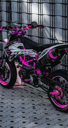 a pink and black dirt bike parked next to a fence