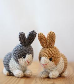 two small knitted rabbits sitting on top of a wooden table next to each other