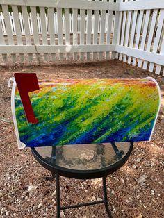 a painted mailbox sitting on top of a table in front of a white fence