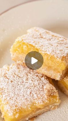 three pieces of lemon bars on a plate with powdered sugar around the edges and one piece cut in half