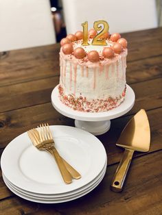 a birthday cake sitting on top of a wooden table next to plates and gold utensils