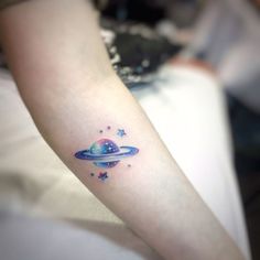 a small saturn tattoo on the left inner arm, with stars and planets around it