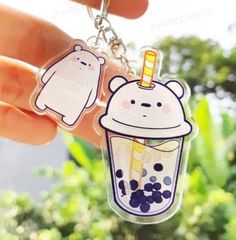 a hand holding a keychain with two bears on it and a drink in the middle