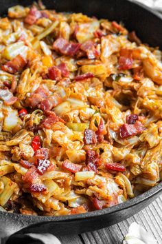 a skillet filled with pasta and bacon on top of a wooden table