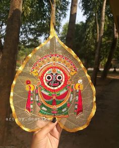 a hand holding up a decorative item in front of some trees and palm tree branches