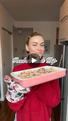 a woman in a red sweater is holding a pink tray with food on it and smiling at the camera